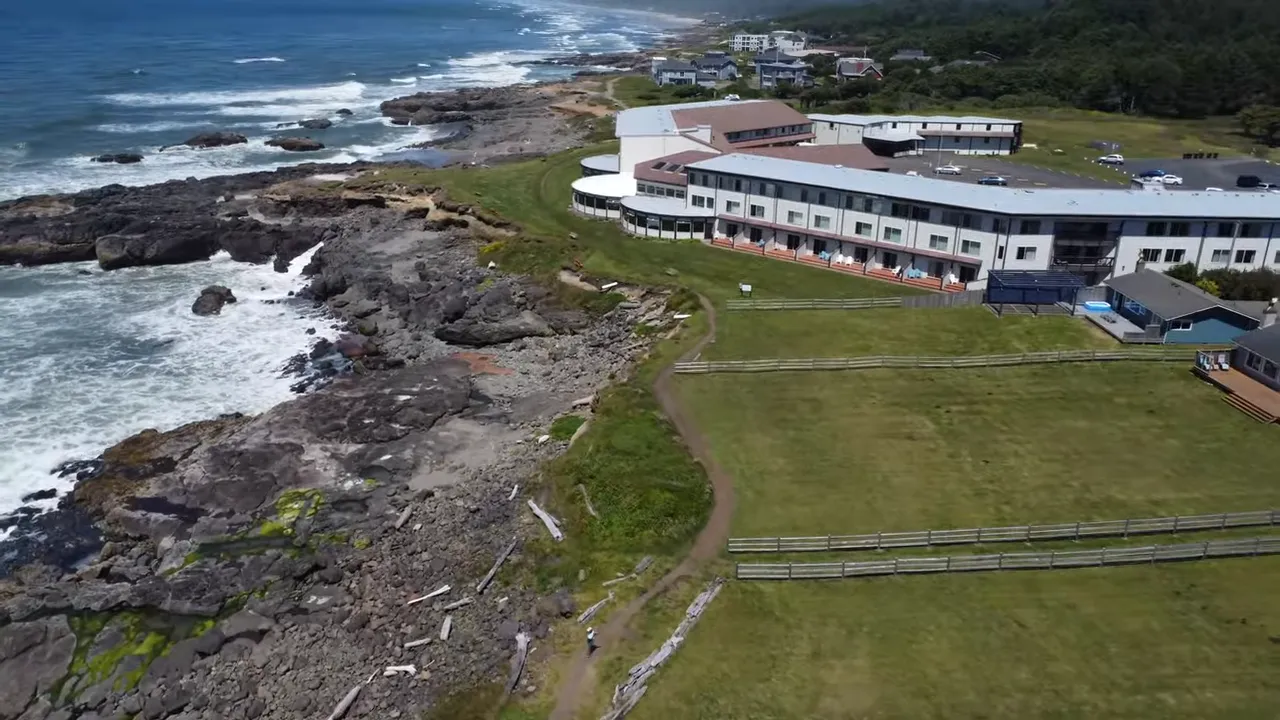 Rocky shoreline with ocean waves beside a long coastal building and grassy grounds