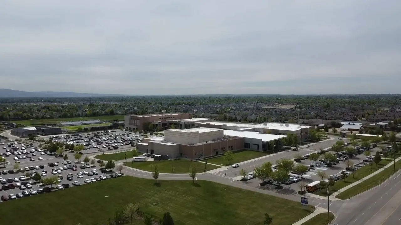Wide aerial photograph of a Meridian school campus showing the main building, parking lots, a school bus and nearby residential area