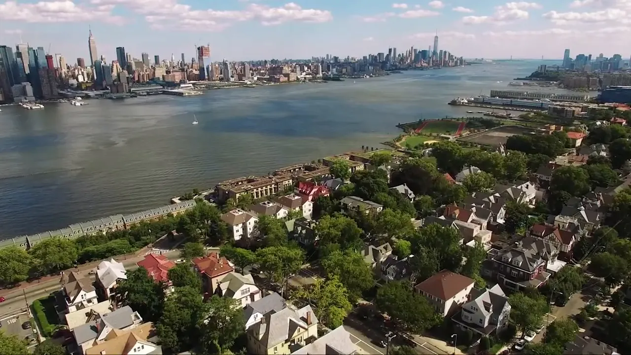 Aerial view of residential neighborhood along the river with city skyline visible across the water