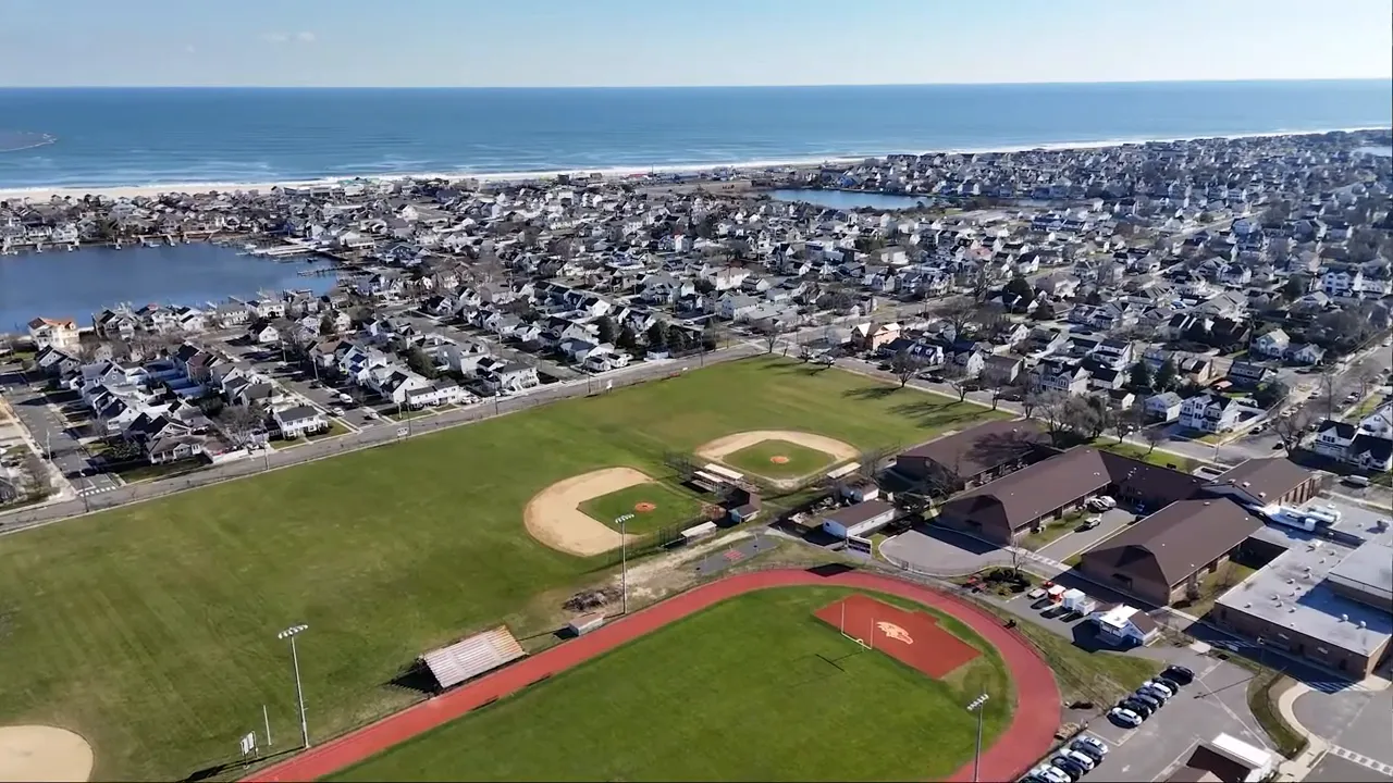 Sharp aerial image of a running track, baseball diamonds, adjacent school buildings, and the nearby ocean.