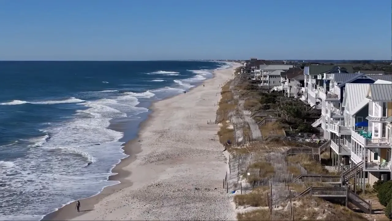 Aerial view of a long sandy beach with waves and beachfront houses along dunes