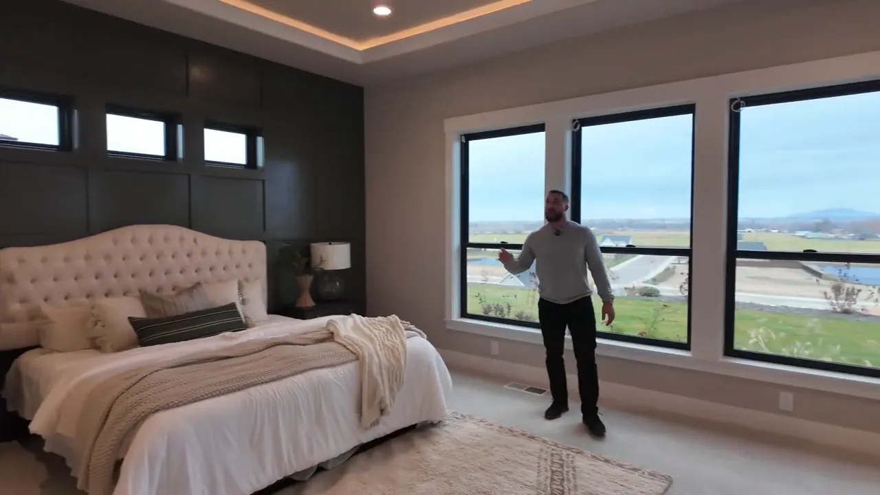 Primary bedroom with dark accent wall large windows and tray ceiling lighting
