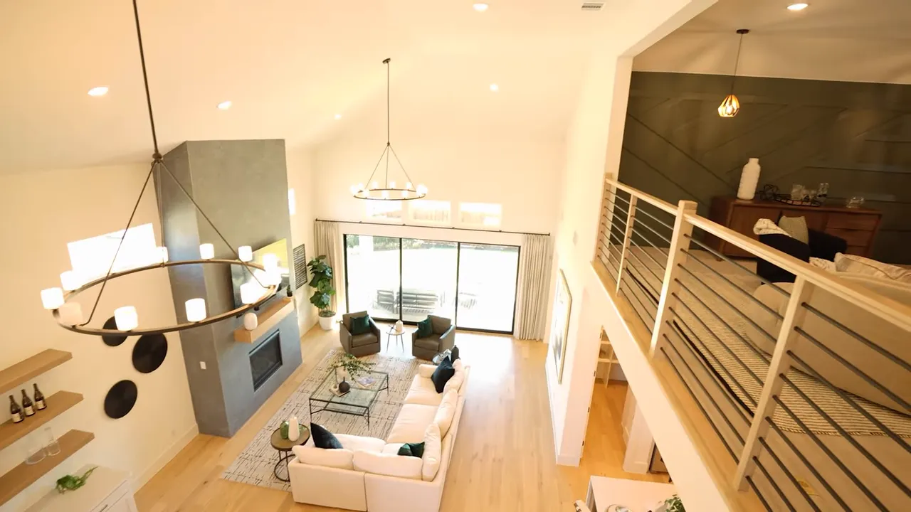 Clear view from the upstairs balcony over the living room showing chandelier, fireplace, sectional and sliding glass doors
