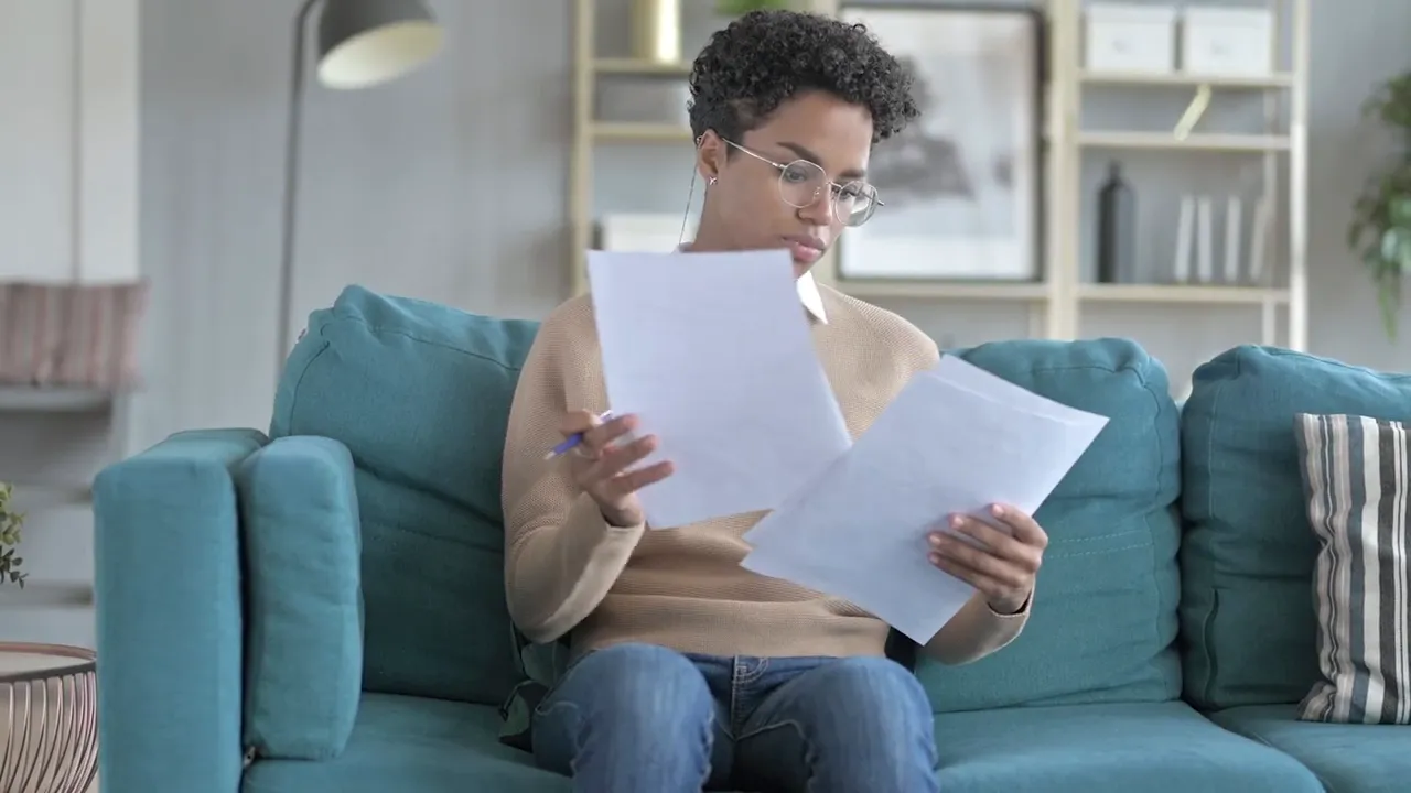 Person on a couch reviewing multiple home-related documents