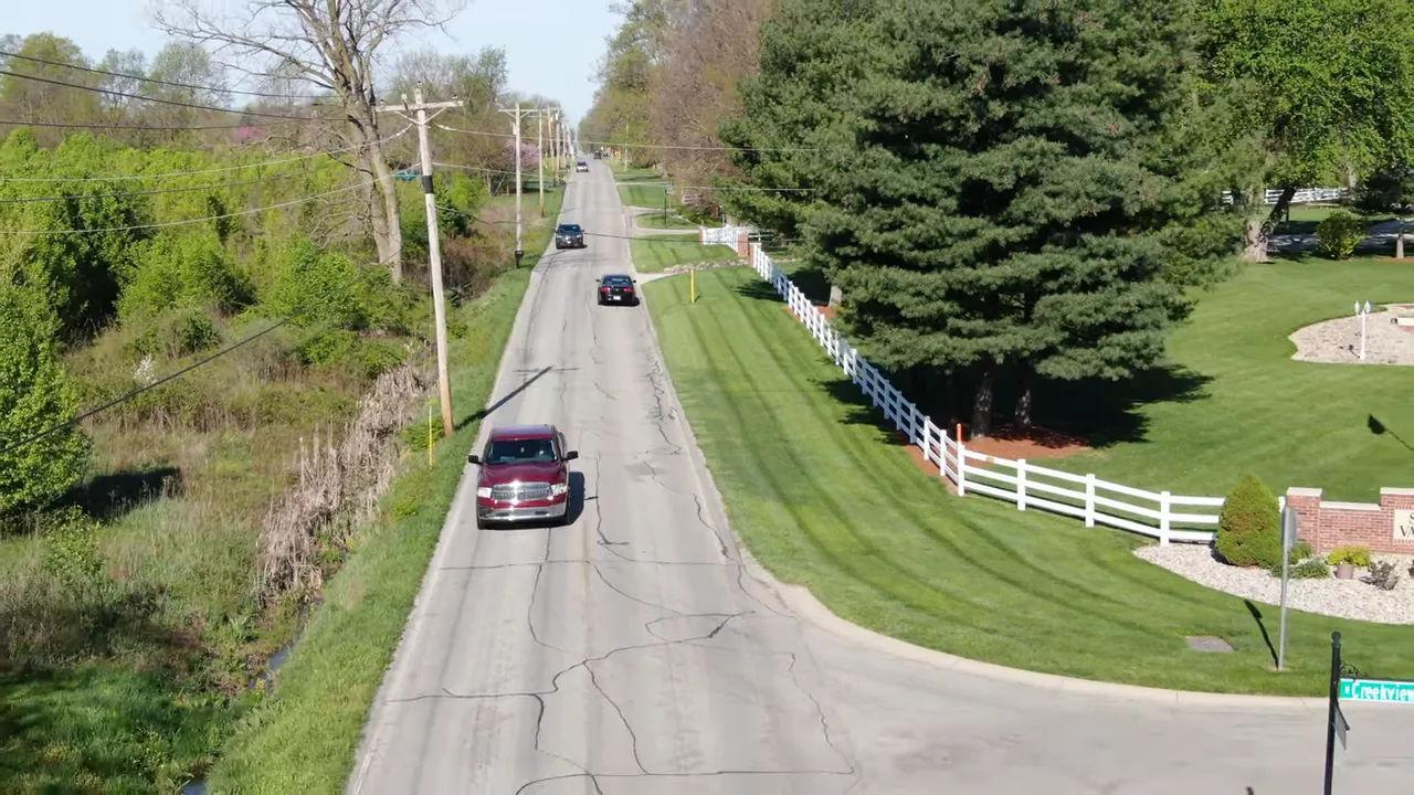 Aerial view of straight two lane road with passing cars and homes set back on large lots