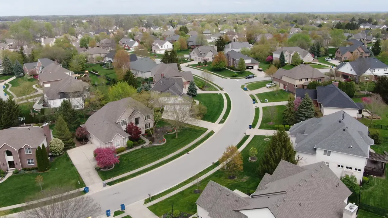 Aerial view of curving suburban streets, sidewalks, and detached homes with large yards