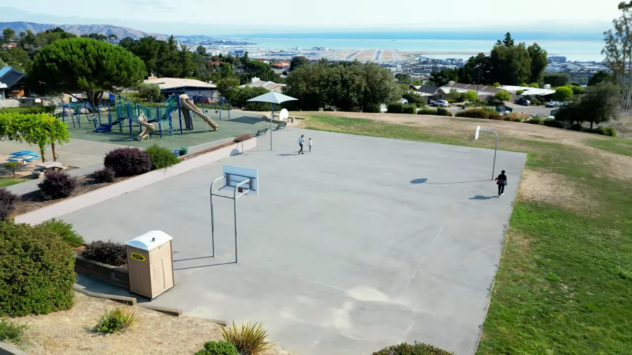 Aerial view of a park playground and basketball court with the bay and an airport runway visible in the distance