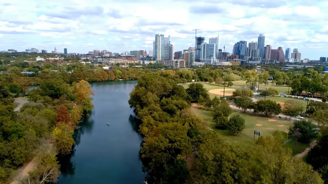 Aerial view of tree-lined creek and trail with Austin skyline in distance