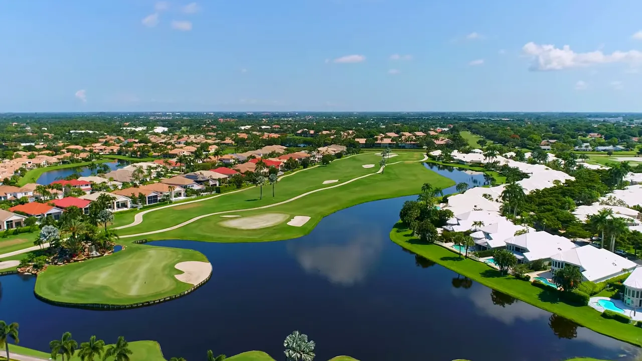 Aerial view of a golf course with an island green, water hazards and surrounding residential homes showing the community scale