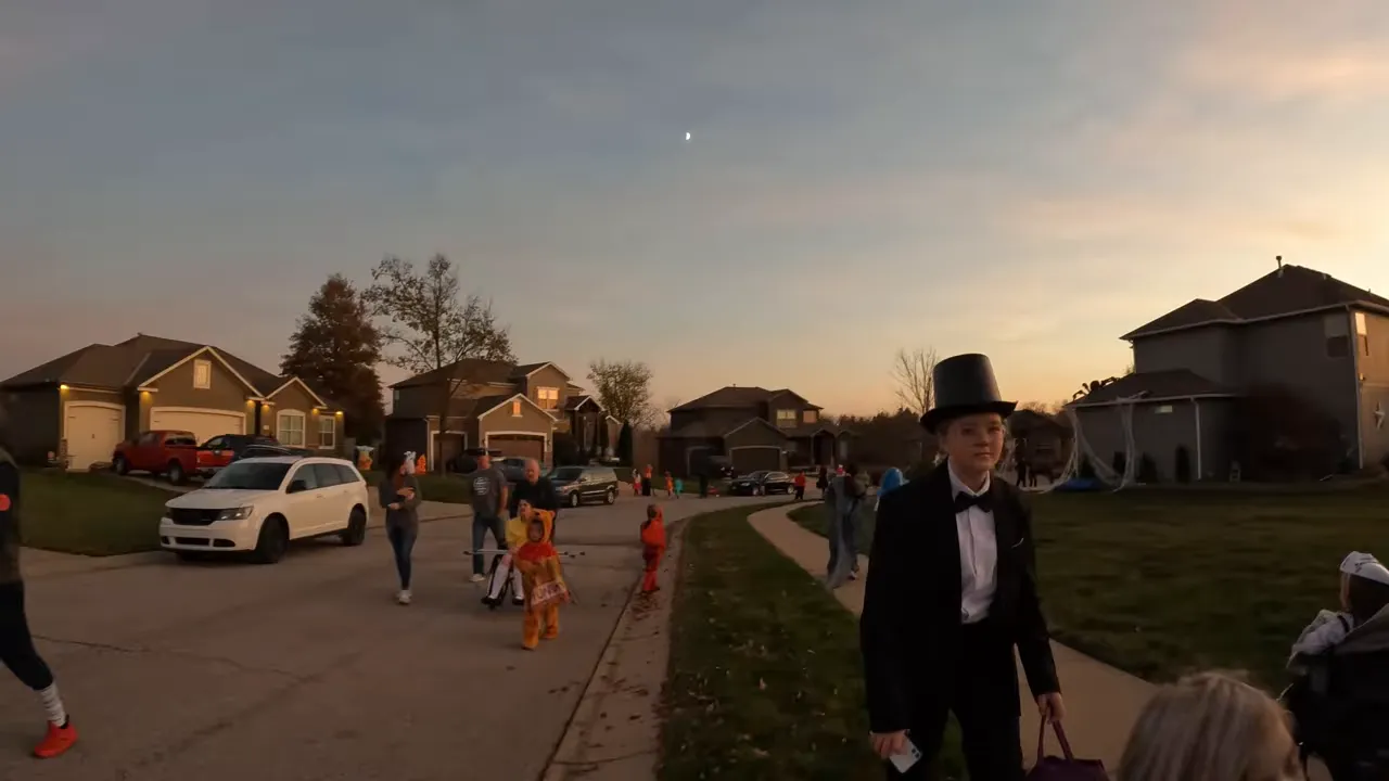 Children in costumes trick-or-treating along a Cayhill neighborhood street at sunset
