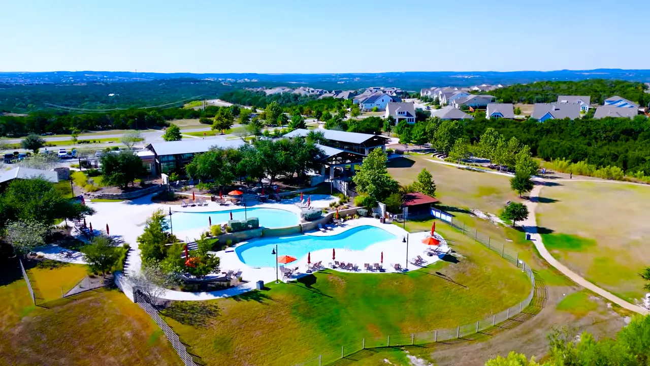 High‑resolution aerial showing Headwaters club amenity, two pool basins, poolside seating, fenced lawn and adjacent walking paths