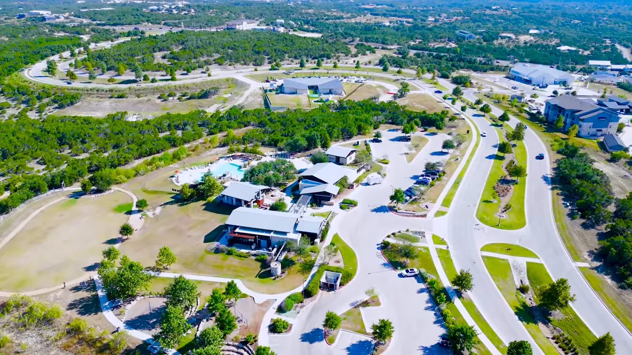 High-angle aerial showing Headwaters amenity buildings, resort pool, parking, trails and surrounding roads and open space