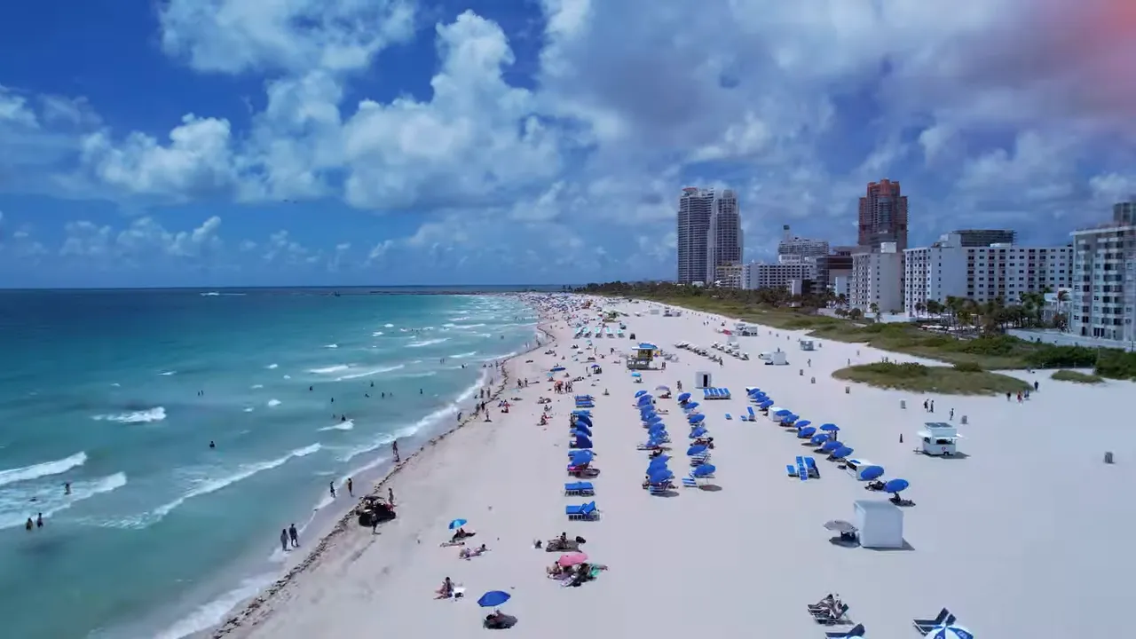 Aerial view of sandy beach with rows of umbrellas and blue ocean on a sunny day