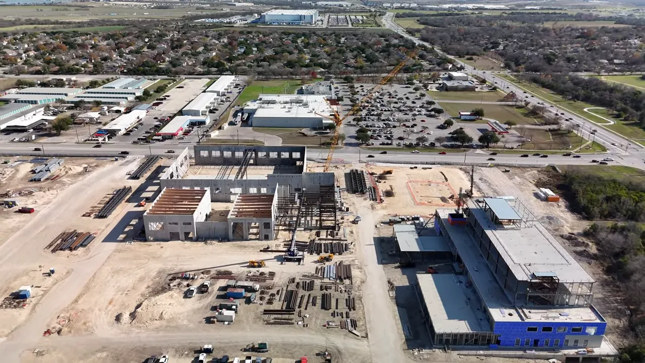 Aerial drone photo of a large construction site and surrounding Austin suburb showing buildings under construction and nearby neighborhoods