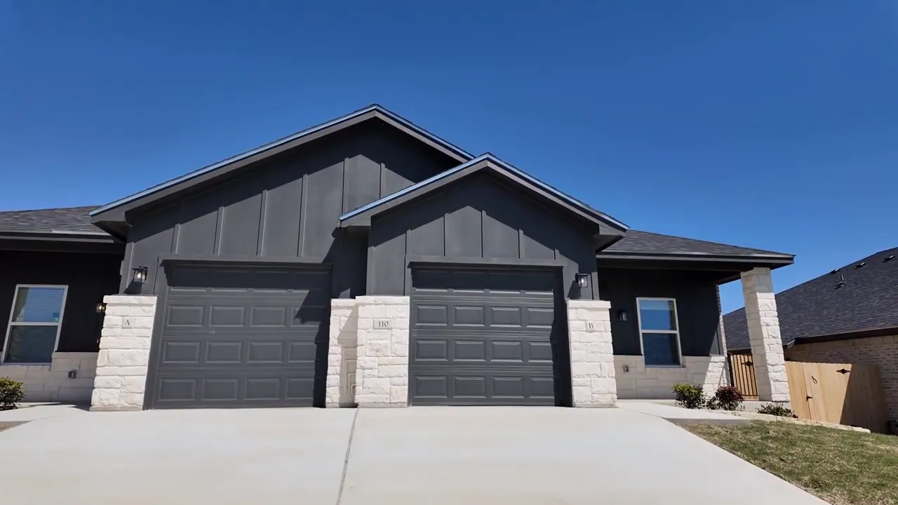 Front exterior view of the Heritage Place duplex at 110 Leon Drive showing garage doors and stone accents