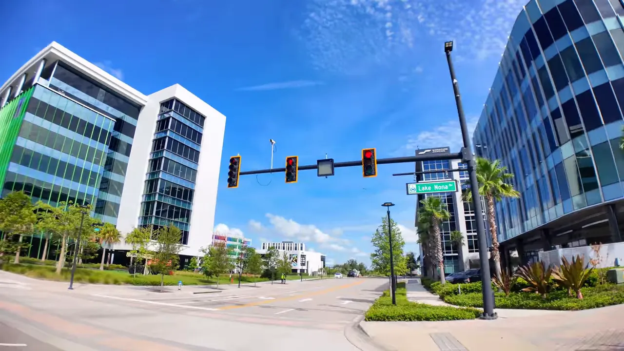 Modern office buildings and traffic lights in a business park with a 'Lake Nona' street sign under a blue sky