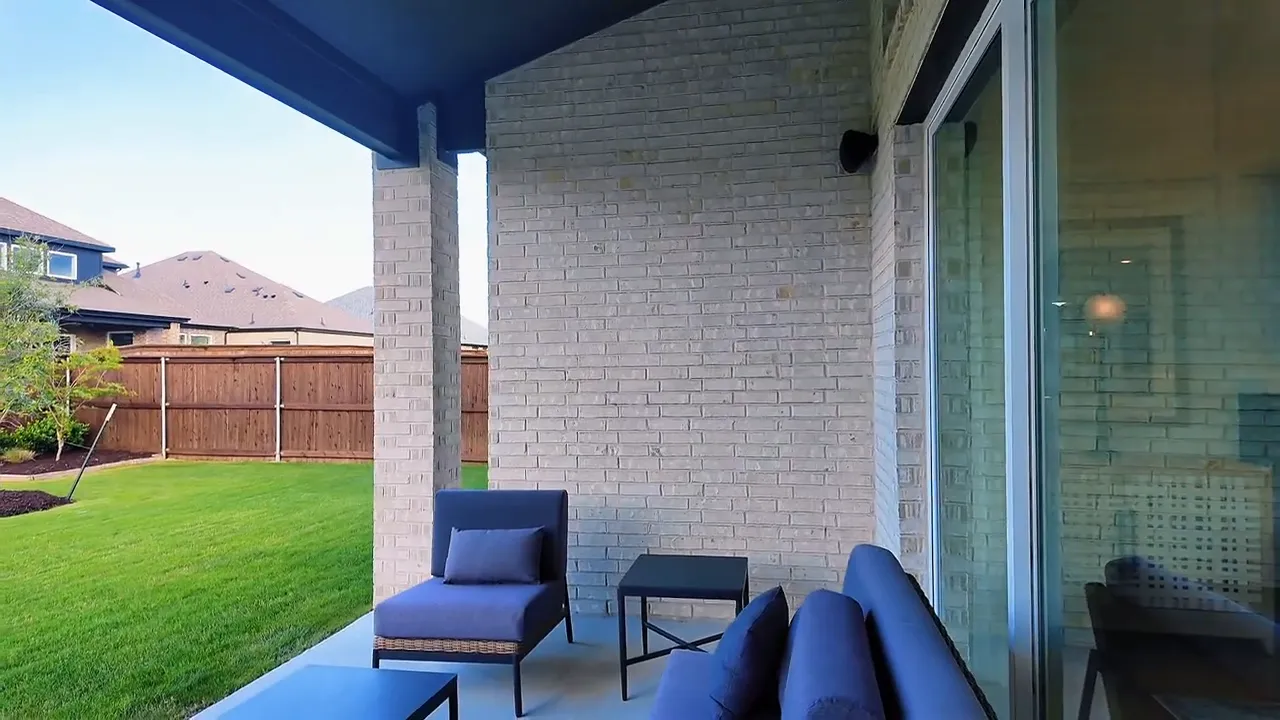 Covered patio seating area on a Forney TX new construction home with brick exterior and backyard view