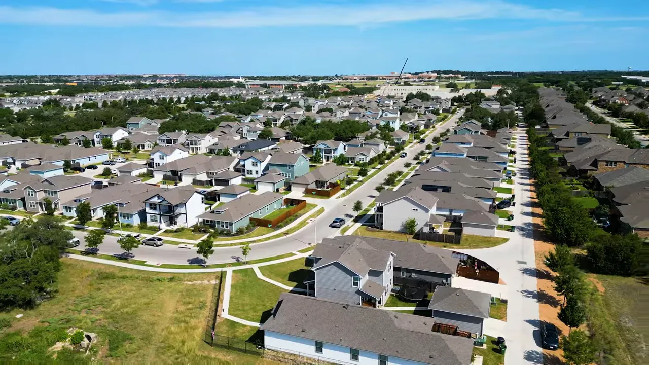 Wide aerial drone photo of a planned suburb with single-family homes, driveways, tree-lined streets, and clear lot boundaries.