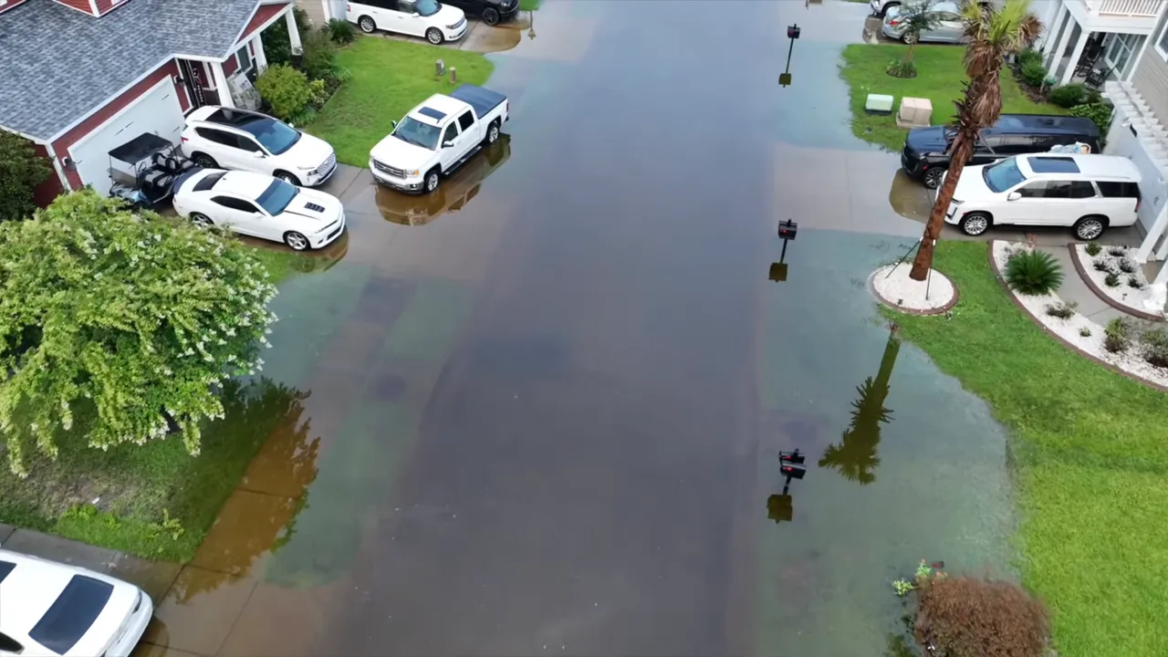 High-resolution aerial photo of a residential street with standing floodwater extending into driveways and lawns.