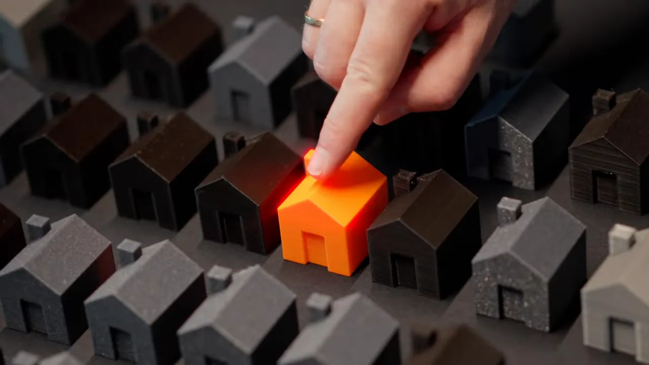 A finger selecting an orange model house among many dark model houses, representing choosing a home.