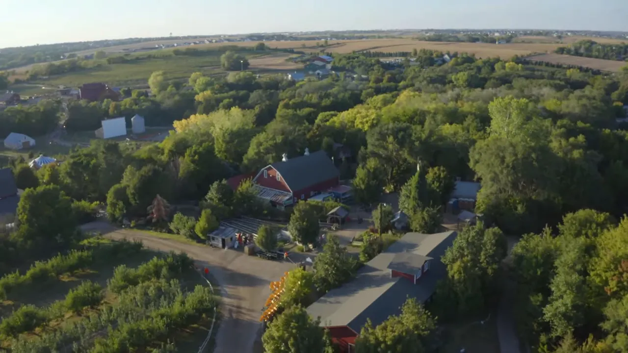 Drone view over tree-lined suburbs, fields, and a red-roofed barn building