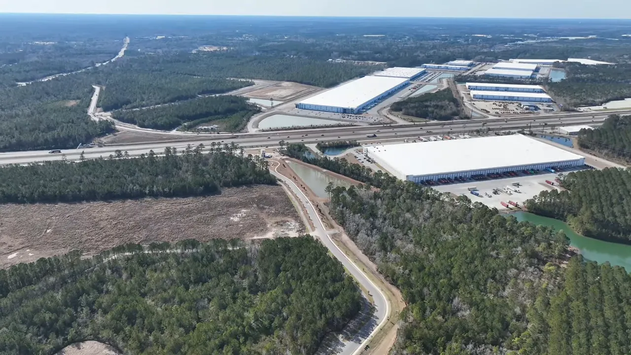 Aerial view showing Highway 26, large warehouses, and connecting roads near wooded areas.