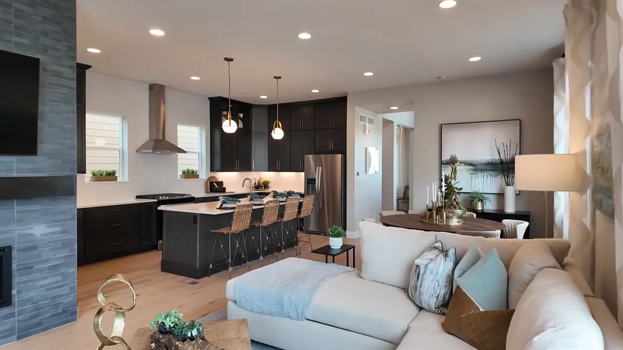 Bright open living room in Painted Prairie Residence 3 model home with wide-plank flooring, fireplace, and modern kitchen view