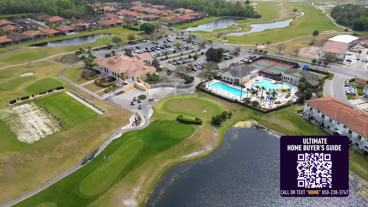 Aerial view of a community clubhouse with large pool, tennis courts, golf greens and a lakeside setting.