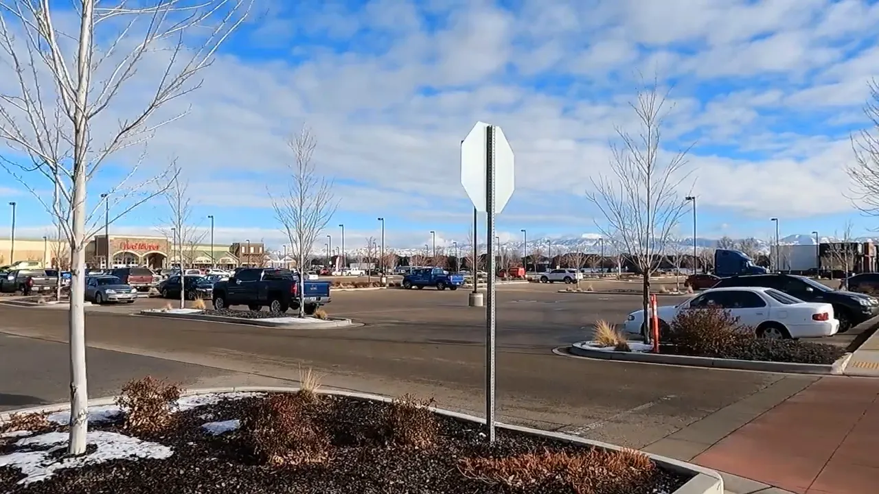 Open parking lot with cars and storefronts in the distance
