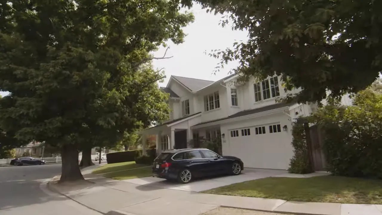 Residential street view with large mature trees shading a driveway and front yard in San Mateo County