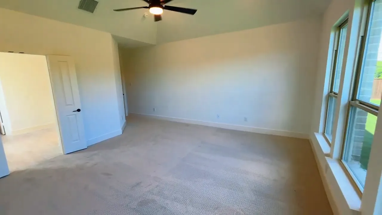 Primary bedroom with large windows carpet and ceiling fan