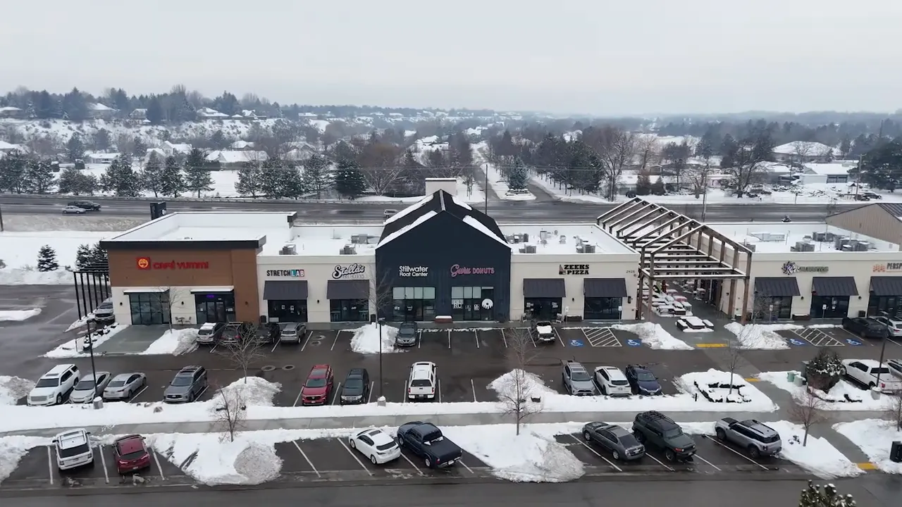 Aerial view of a retail strip center in winter with multiple storefronts and parked cars