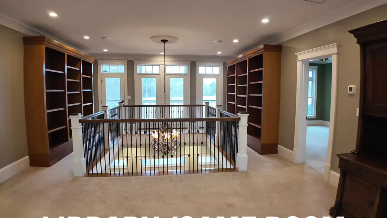 Spacious upper-level library and game room with symmetrical built-in bookshelves, balcony railing and chandelier over the foyer