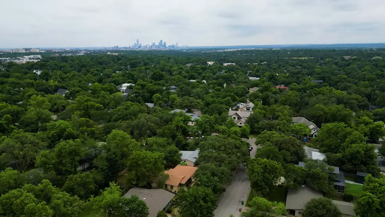 Aerial view over dense green neighborhood toward distant skyline
