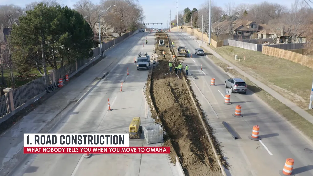 aerial view of road construction with crews, machinery, and orange traffic barrels down the center of a street