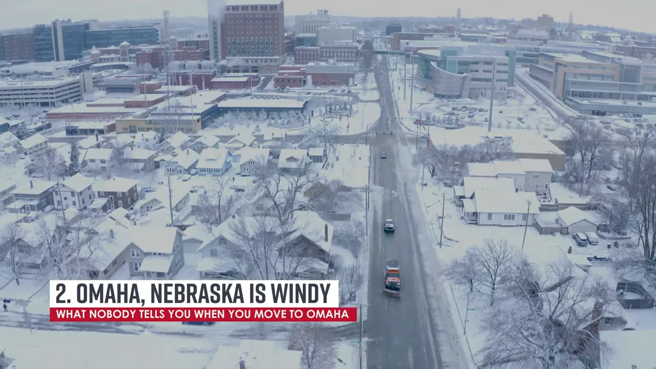 Aerial view of snowy Omaha neighborhood with snowplows on the road and on-screen text '2. Omaha, Nebraska is Windy'.