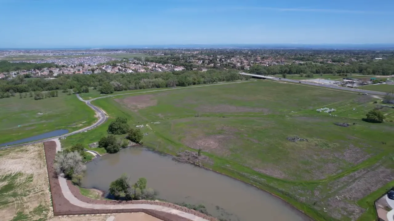 Aerial view of large open fields with a pond and distant neighborhoods in Roseville