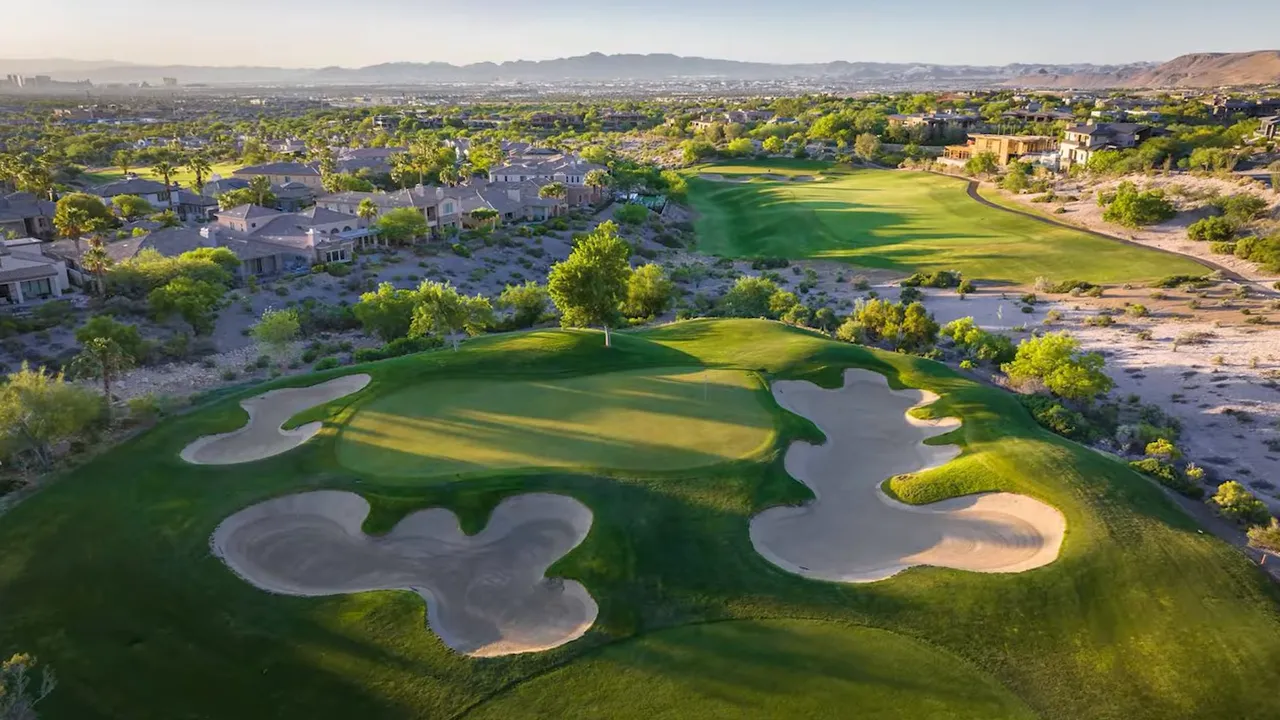 Green golf course with sand bunkers and mountains in the background