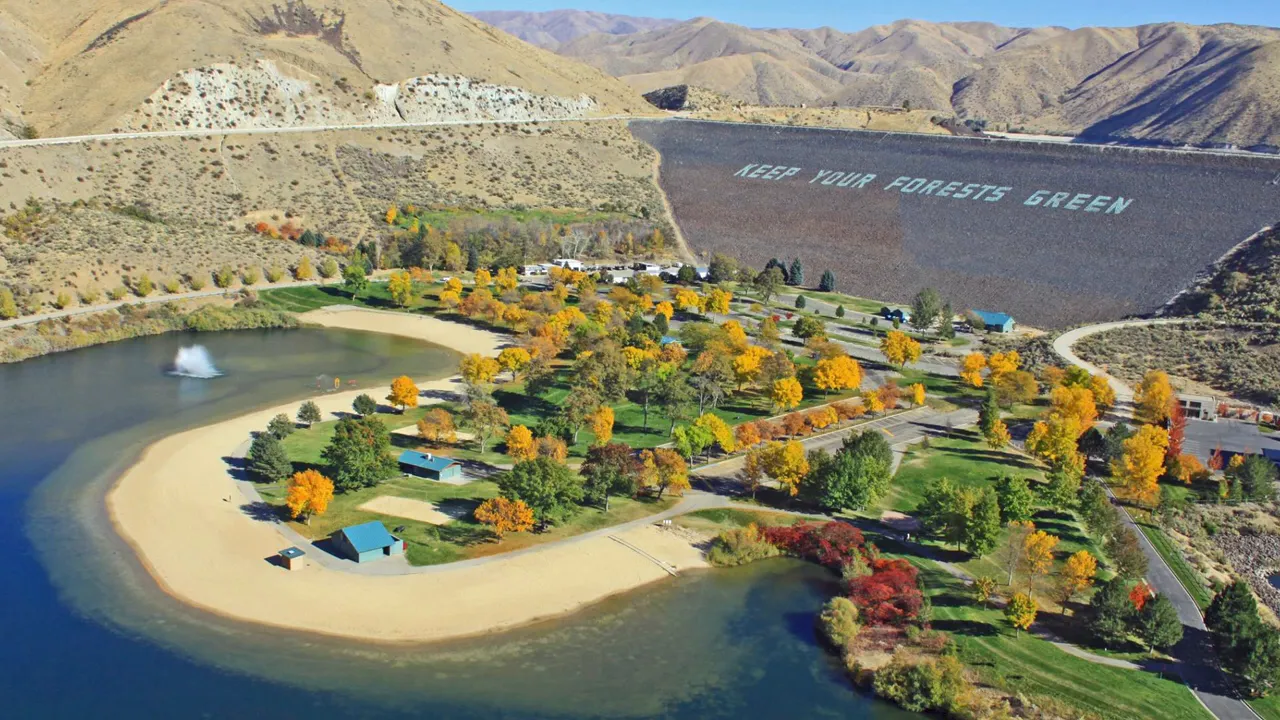 Aerial view of sandy shoreline, water, trees, and Lucky Peak Dam