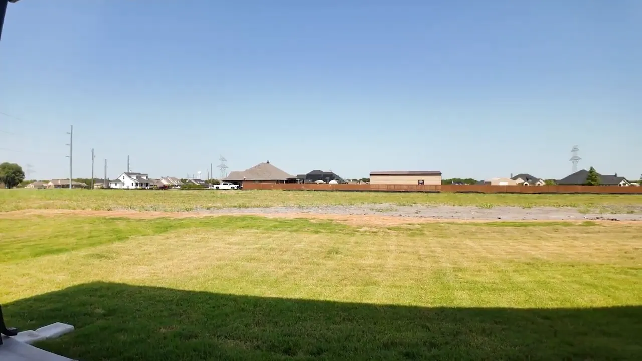 Backyard view from covered patio showing wide grassy acre lot and open space