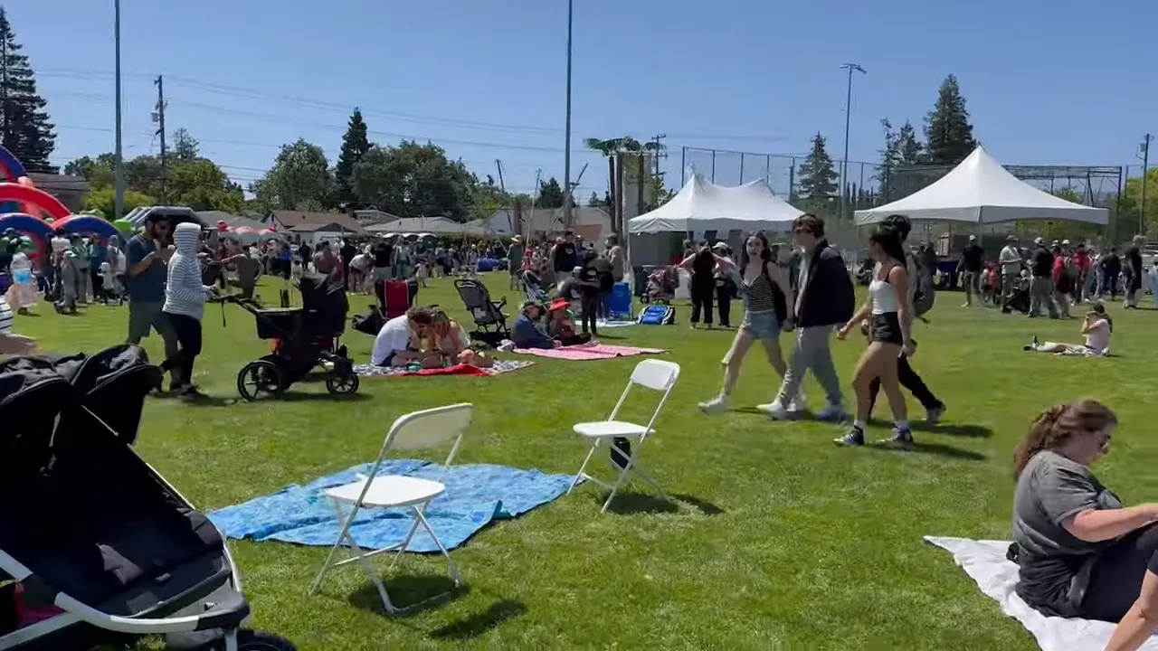 People gathered at an outdoor community event with tents and families in a grassy field