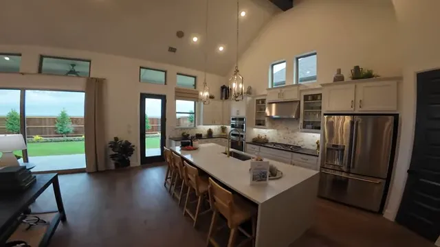 Open kitchen with white island and bar stools beside living room with tall windows