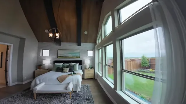 Primary bedroom with vaulted wood-beam ceiling, tall windows, bed, and backyard view