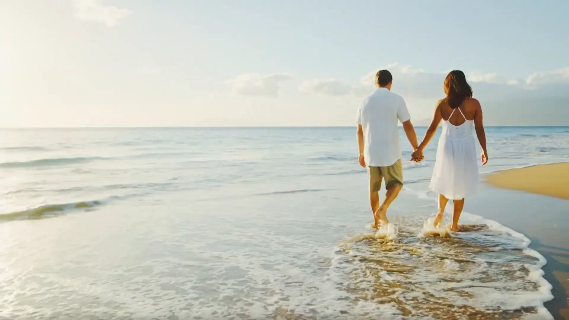 Couple walking hand-in-hand along a sunny beach with gentle waves