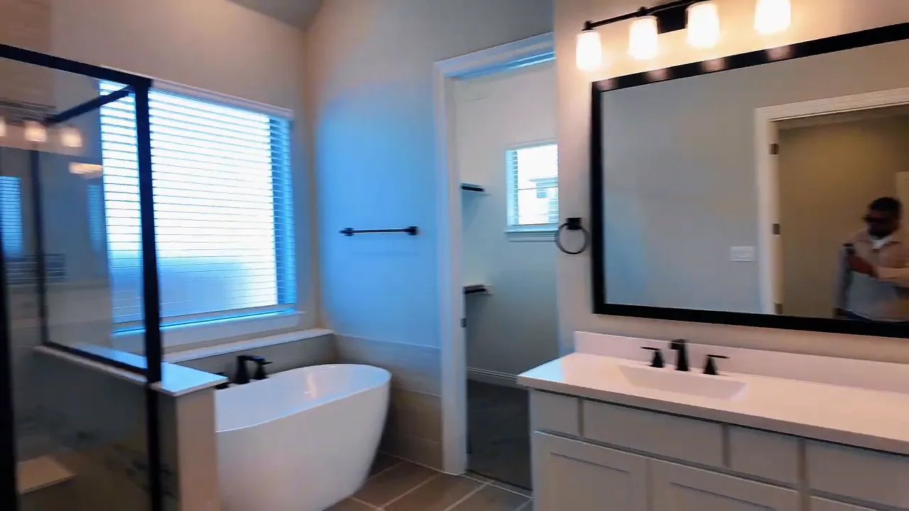 Primary bathroom vanity with double sinks, light fixtures, and large window in a new construction home near Dallas TX