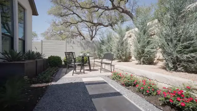 Landscaped side yard with stone pavers flower bed chairs and mature trees