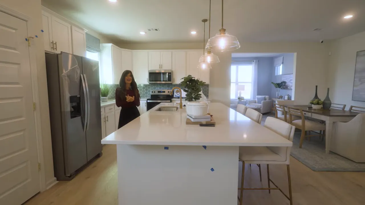 Open-plan kitchen with long white island, pendant lighting, dining area visible in the background.