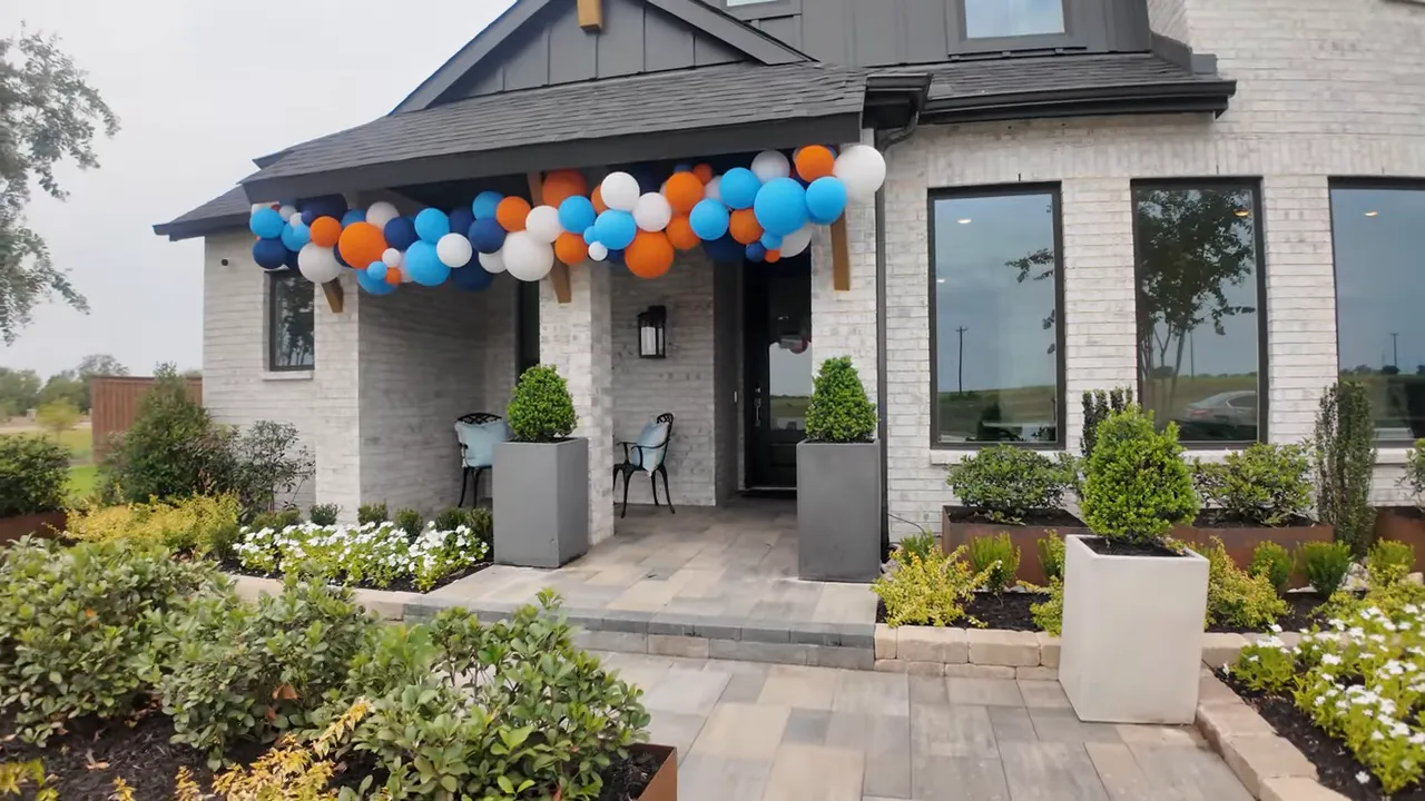 Front exterior of white brick model home with balloon garland over porch and landscaped entry