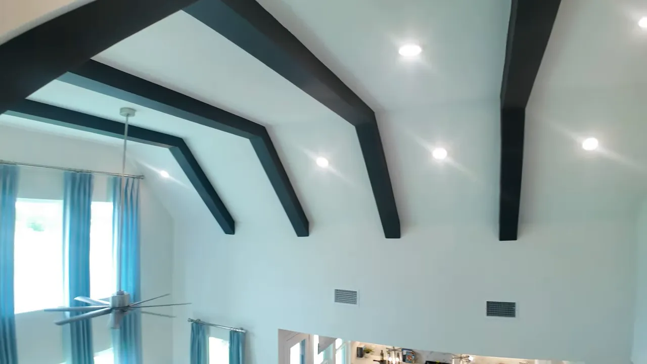 Vaulted white ceiling with dark decorative beams and recessed lights above living room
