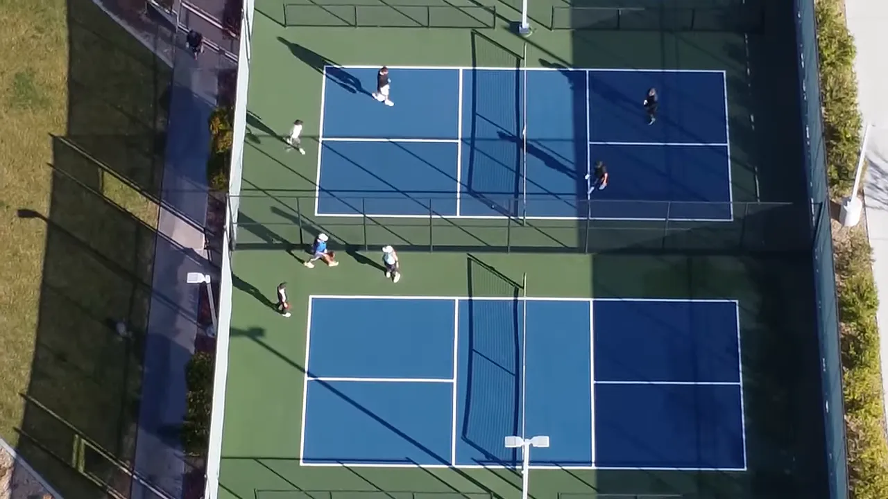 Overhead view of several occupied blue and green pickleball courts